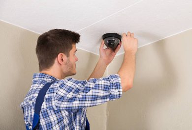 Young Male Technician Installing Surveillance Camera On Ceiling